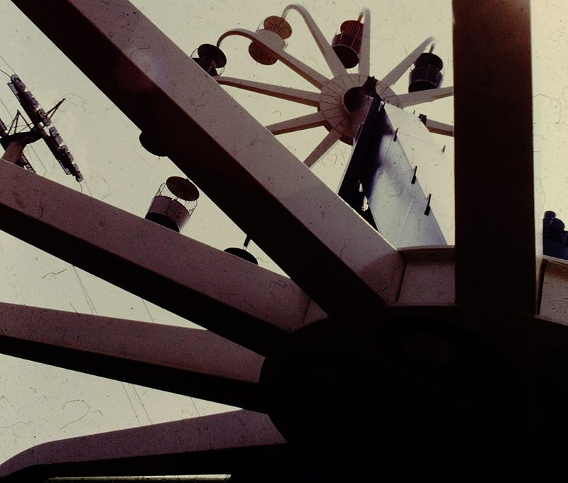 Photo of Giant Wheel taken from a cabin near the ground, with the other wheel high in the sky. Another ride, Sky Ride can be seen nearby, with its cables passing through the area.